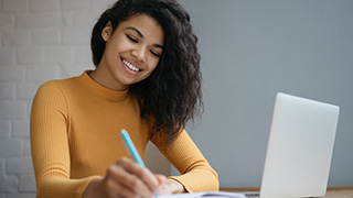 Student writing in a notepad in front of a computer.