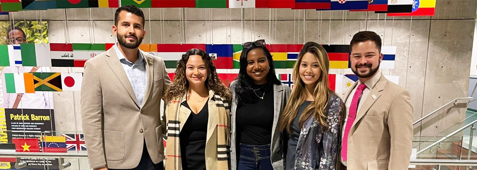 Image of members of the Joseph A. Unanue Latino Institute Alumni Committee in front of a staircase with flags. 