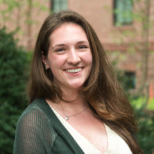 Kiersten Lynch wearing a green sweater and standing in front of a brick building