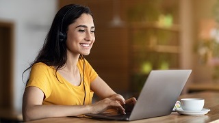 Student sitting in front of an open laptop screen writing in a notepad with a pen. 