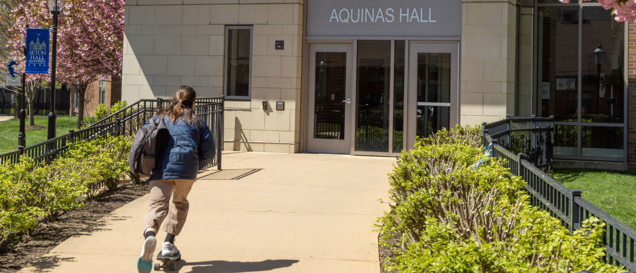 Aquinas Hall with a student skateboarding into it. 