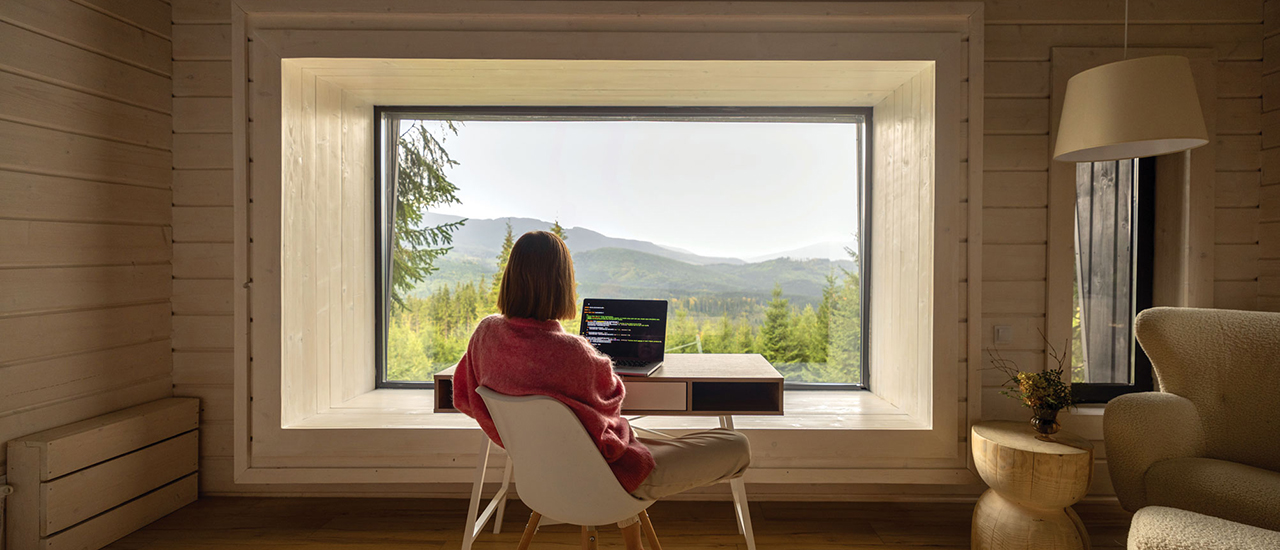 A photo of a person sitting in front of a window working on a computer,