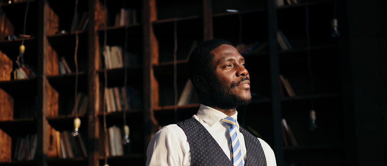 A person standing in front of bookcases with a thoughtful expression on their face.