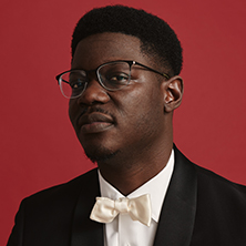 Edmund Adjapong in a gray suit sitting on stairs