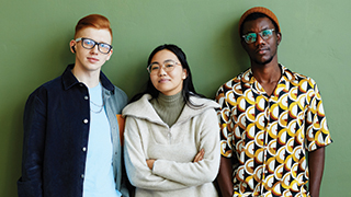 Three diverse gen z employees posing against a green wall.