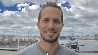 A man with a beard smiling in front of a cityscape