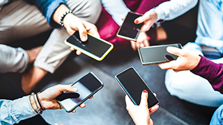 People sitting in a circle holding out their cell phones.