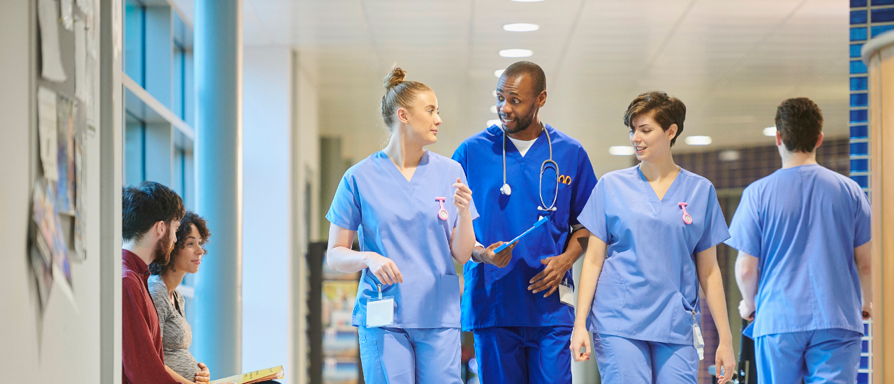 A group of nurses walking through a hallway surrounded by patients. 