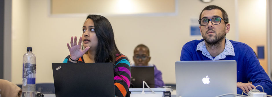 students sitting in a classroom with laptops, asking questions and participating